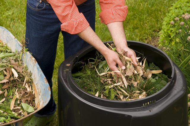 hands placing leaves inside a garden composter